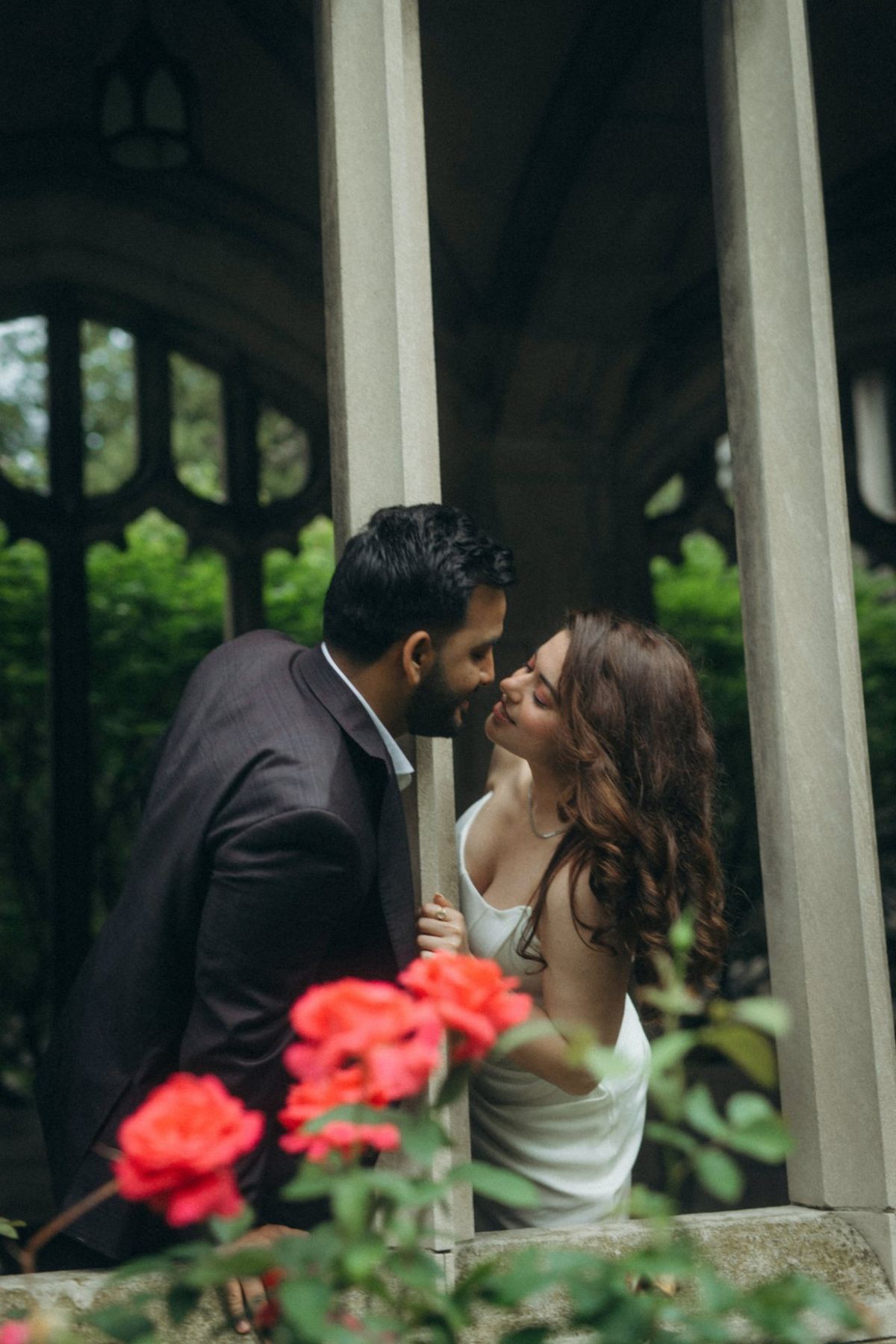 Manpreet and Kanwar between stone columns with red roses in the foreground, e-shoot styling by Bhoomi Jani Weddings