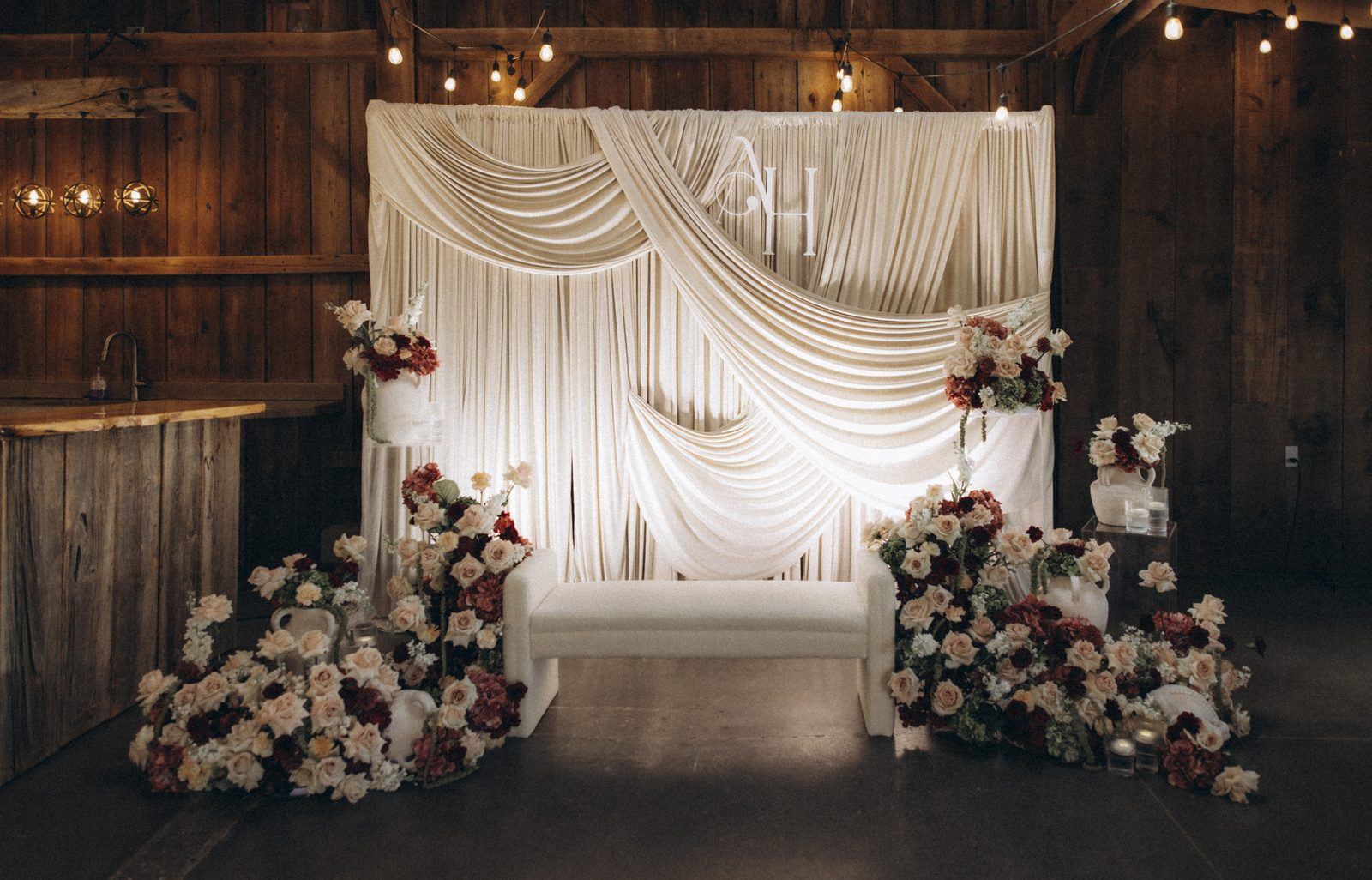 Draped ivory backdrop with blush and burgundy florals in a barn venue, wedding design direction by Bhoomi Jani Weddings, Greater Toronto Area